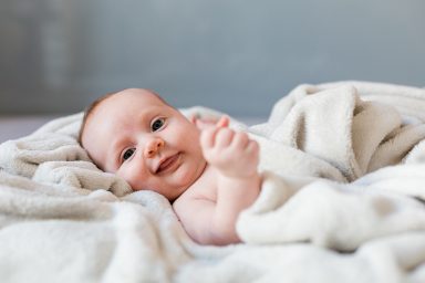Lächelnder Baby liegt auf einer weichen Decke.