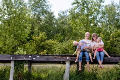 Vier Personen sitzen entspannt auf einem Holzsteg inmitten von Bäumen.