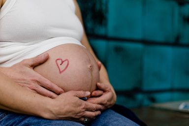 Schwangere Person hält ihren Bauch mit einem roten Herzsymbol darauf.