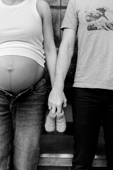 Ein schwangeren Paar hält händchen und eine Babyflasche in der anderen Hand.