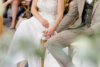 Hochzeitspaar sitzt zusammen, Hände halten sich, romantische Atmosphäre.