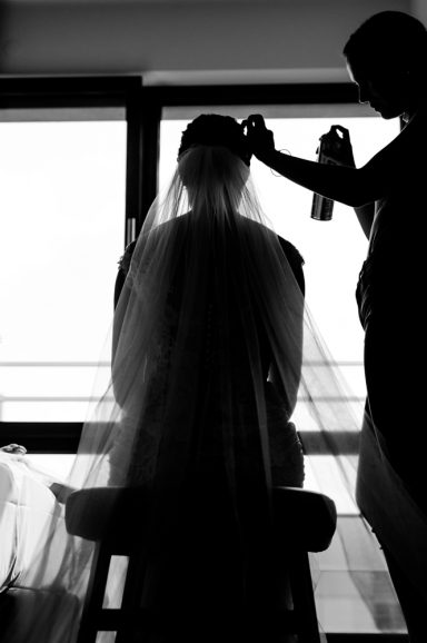 Eine Braut wird in Silhouette mit einem Schleier und Haarspray gestylt.